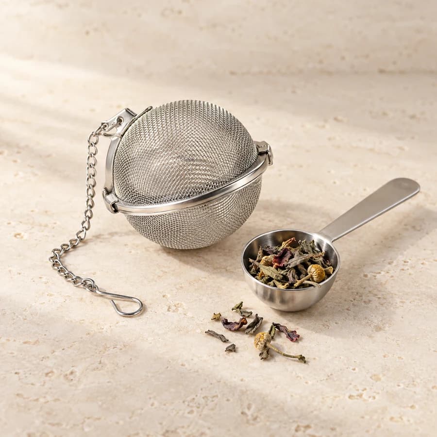Generated product image: A stainless steel mesh tea infuser ball and matching scoop with loose herbs.